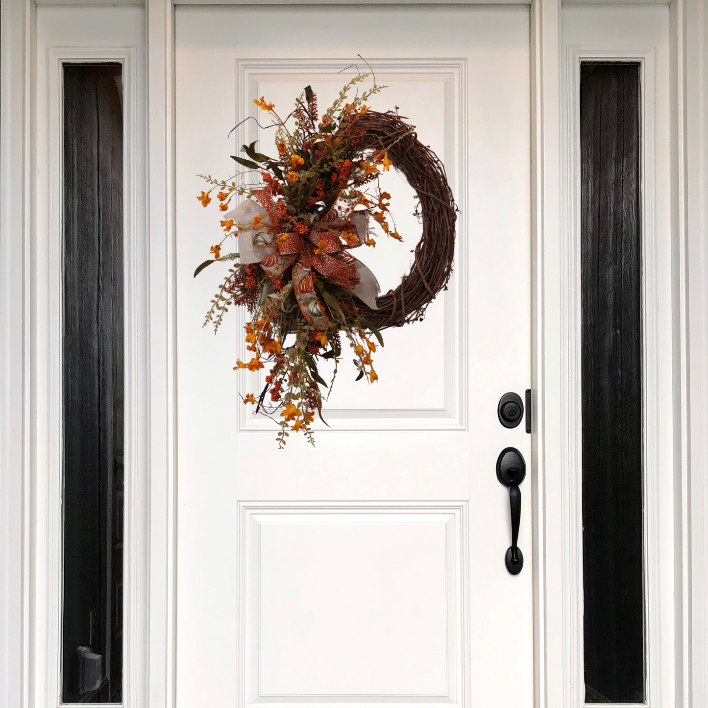Fall grapevine wreath with Orange filler flowers and a large bow with Orange and Sage pumpkins