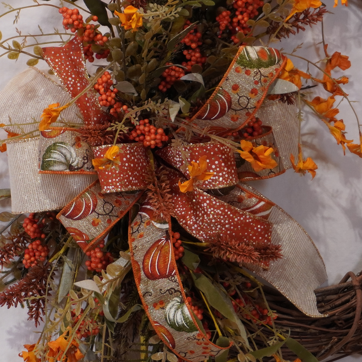 Fall grapevine wreath with Orange filler flowers and a large bow with Orange and Sage pumpkins